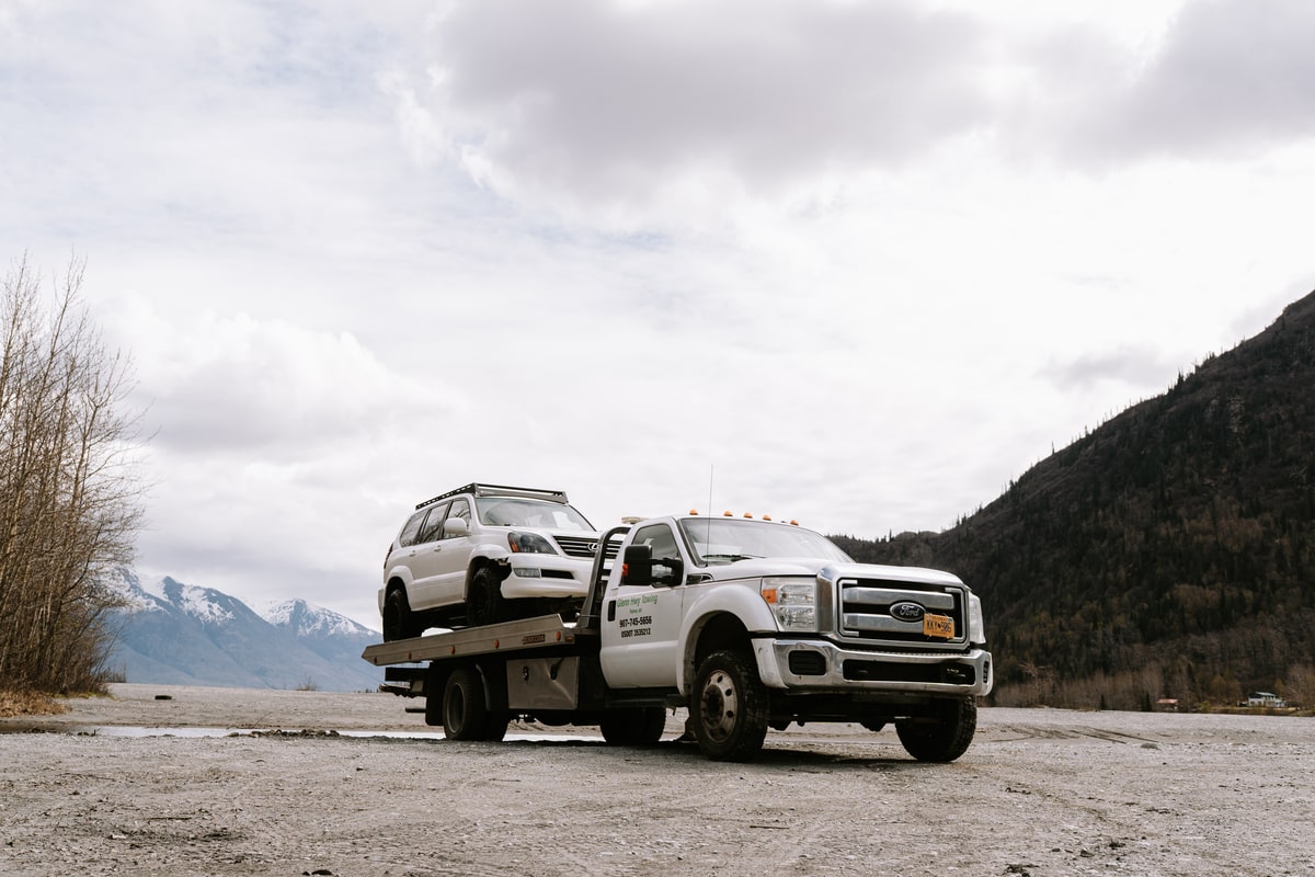 Flatbed tow truck carrying an SUV in an Alaska mountain setting