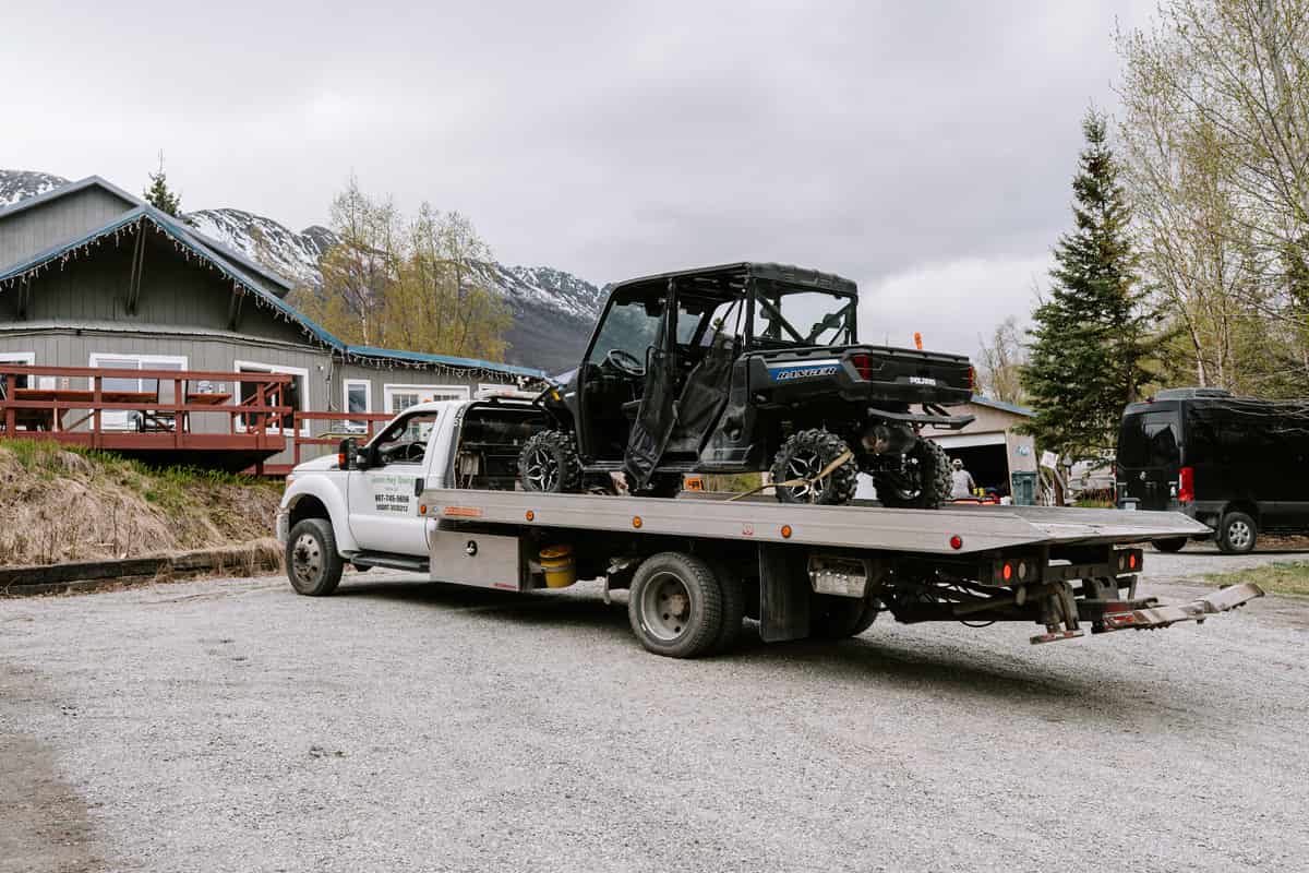 Side-by-side vehicle loaded on a flatbed tow truck in Alaska
