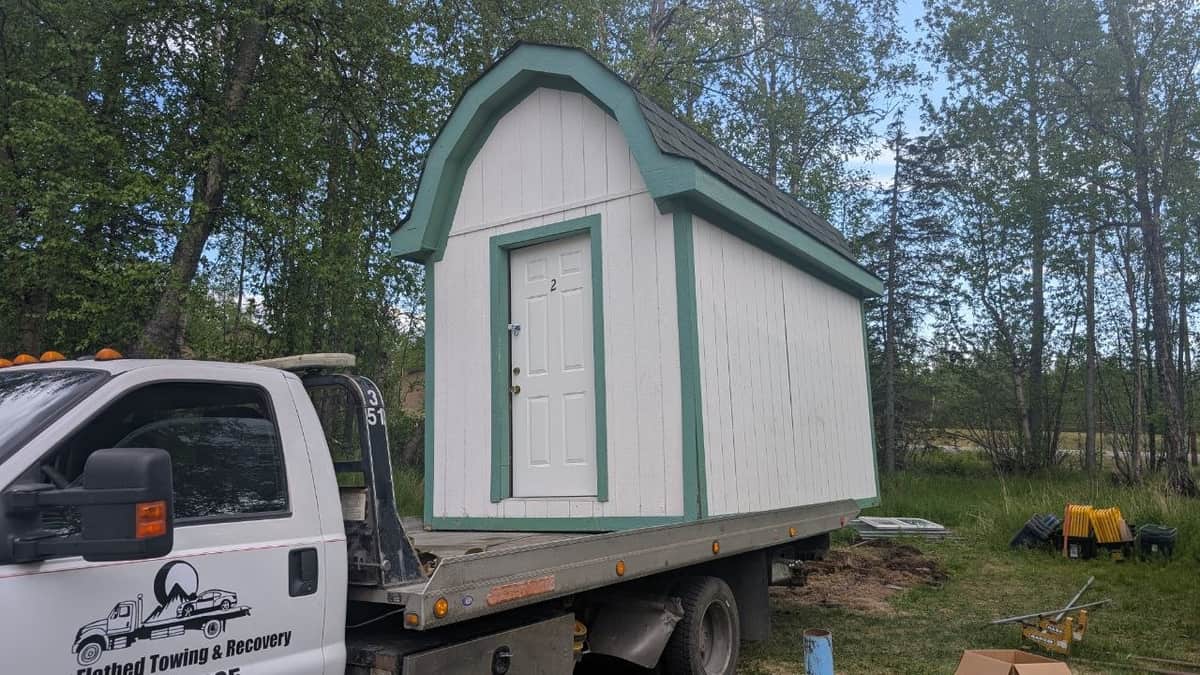 Flatbed tow truck carrying a prefabricated shed for delivery